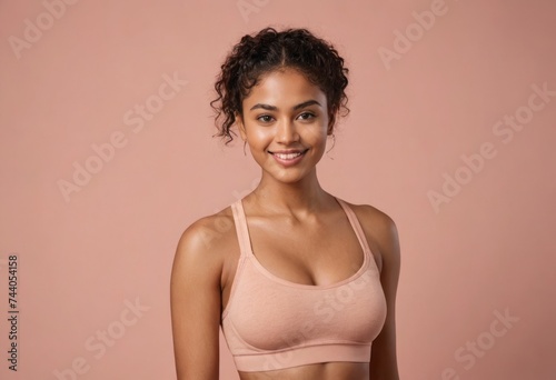 A sporty young woman stands in a neutral-toned sports bra, her posture relaxed and her expression content.