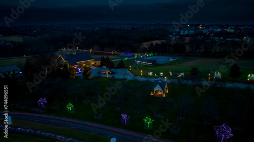 Overhead View Of A Rural Landscape At Twilight Featuring Decorative Holiday Lights On Trees And Structures, With A Small Chapel In The Foreground.