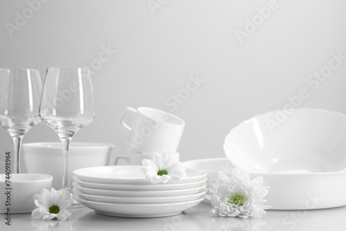 Set of many clean dishware, flowers and glasses on light table