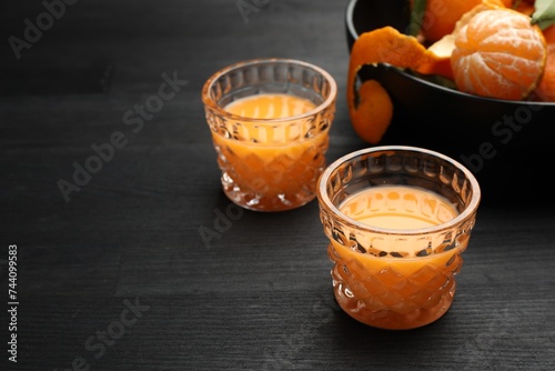 Fototapeta Naklejka Na Ścianę i Meble -  Tasty tangerine liqueur in glasses and fresh fruits on black wooden table. Space for text