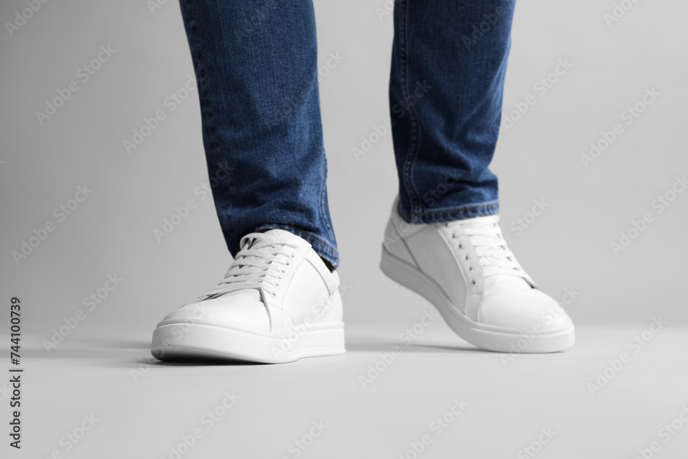 Man wearing stylish white sneakers on grey background, closeup