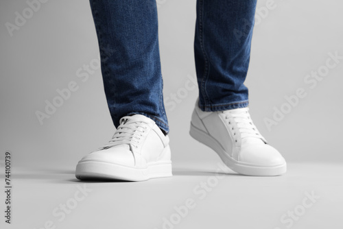 Man wearing stylish white sneakers on grey background, closeup