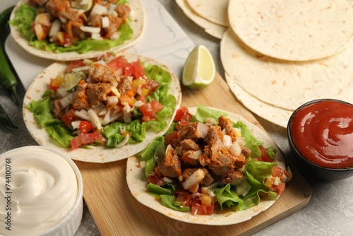 Delicious tacos with vegetables, meat and sauce on grey textured table