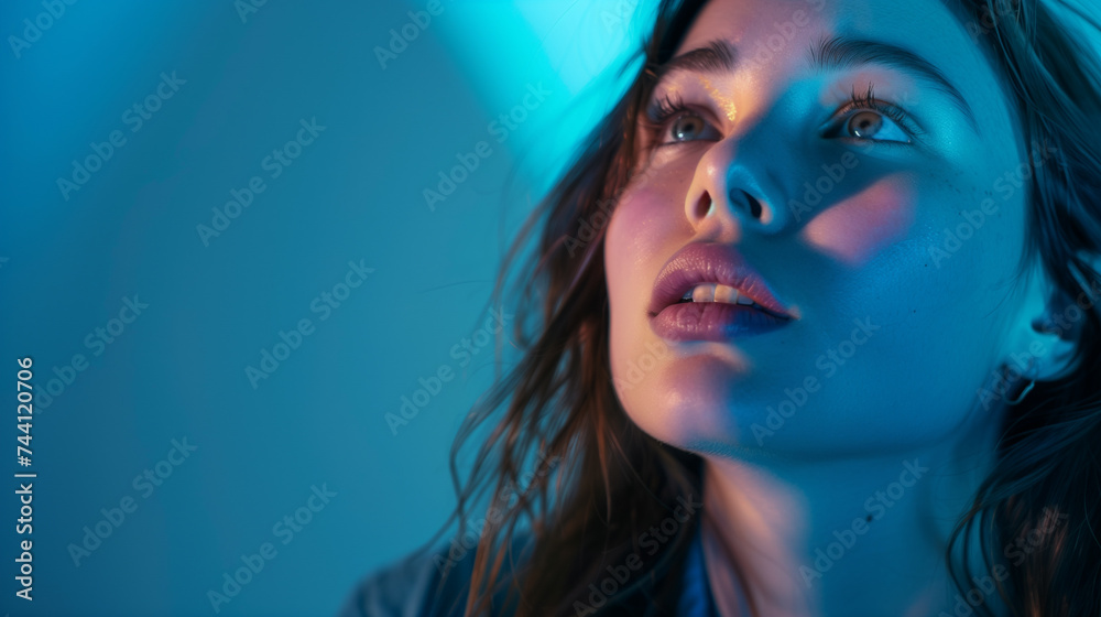 Frightened woman with a horrified expression in dim blue light, depicting fear or anxiety.