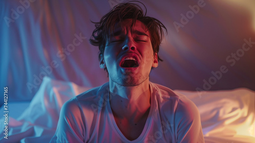 Man experiencing a nightmare, distress or orgasm, sitting in bed with a pained expression, illuminated by eerie red light. photo