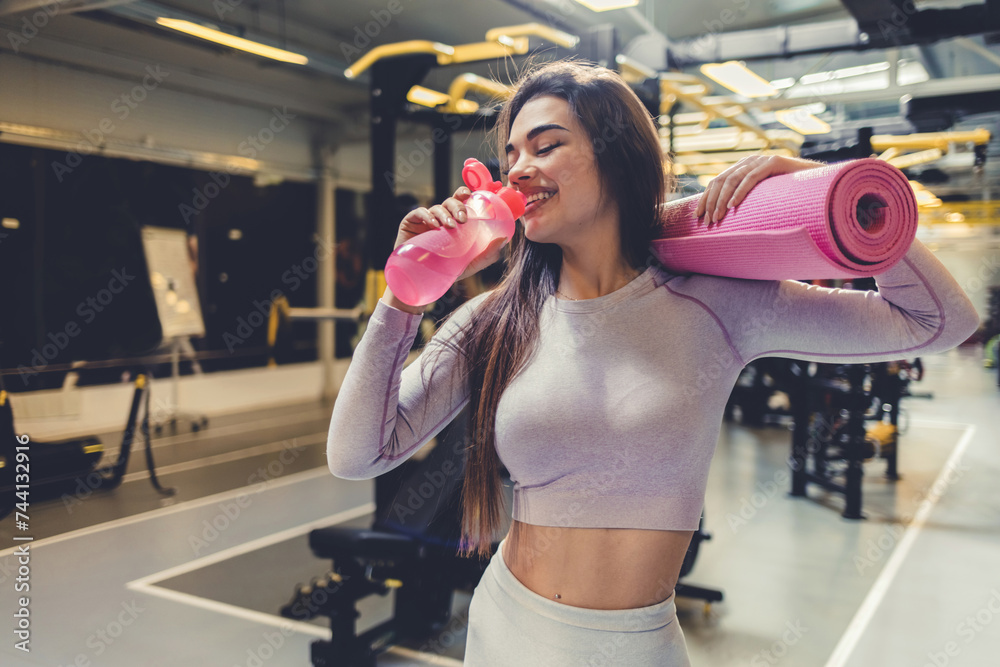 Happy, fitness and healthy while holding exercise mat and water bottle in the gym. Fit woman with slim body after exercise, training and sports workout and vitality healthcare. Happy, fitness and healthy while holding exercise mat and water bottle in the gym. Fit woman with slim body after exercise, training and sports workout and vitality healthcare.
