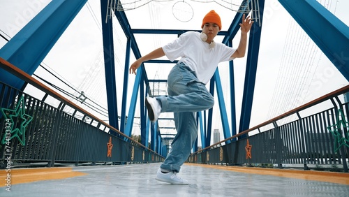 Professional break dancer perform street dance footstep at bridge. Asian hipster wear headphone while doing freeze pose. Break dancer, street dancer freestyle concept. Outdoor sport 2024. Sprightly. © Summit Art Creations