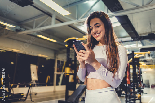 Idea, phone and exercise with a sports woman by a window, standing in the gym during a fitnesss workout. Health, thinking and a female athlete using social media or an app to track her training. photo