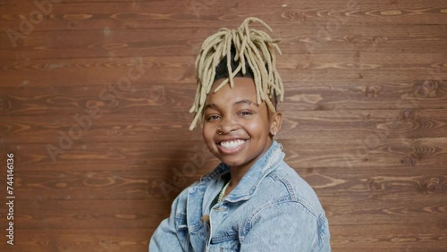 genderfluid person with blonde dreadlocks smiles at the camera with arms crossed in fron of a wooden backdrop wall photo