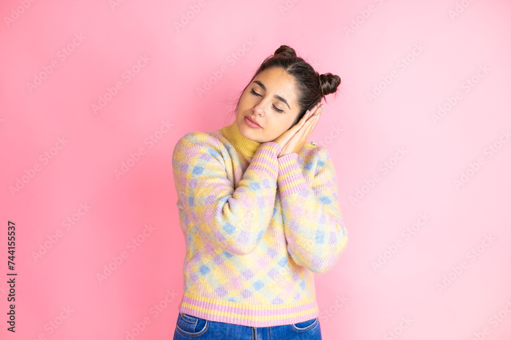 Young beautiful woman wearing casual sweater over isolated pink background sleeping tired dreaming and posing with hands together while smiling with closed eyes. Young beautiful woman wearing casual sweater over isolated pink background sleeping tired dreaming and posing with hands together while smiling with closed eyes.