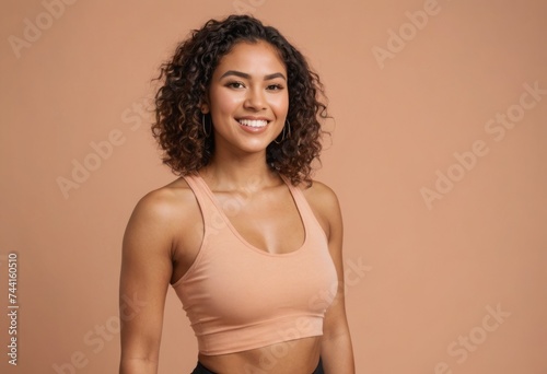 A woman with curly hair and a sports bra smiles warmly, showing her enthusiasm for fitness and a healthy lifestyle.