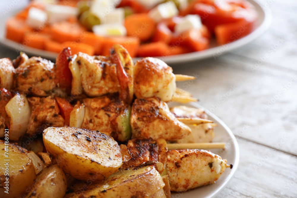 Chicken skewers close-up with vegetables and roasted potatoes.
