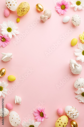 Easter festivity  pastel hues and joyful moments. Top view vertical shot of decorated eggs  ceramic bunnies  white and pink flowers on pastel pink background with space for festive message or promo