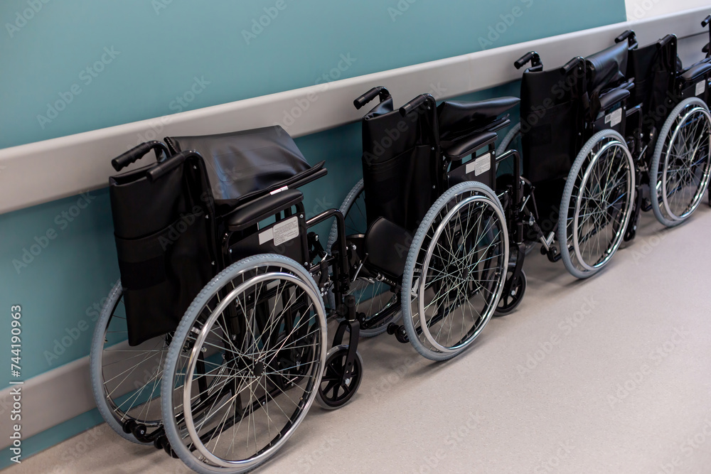 A row of empty folded wheelchairs along a corridor with a blue wall