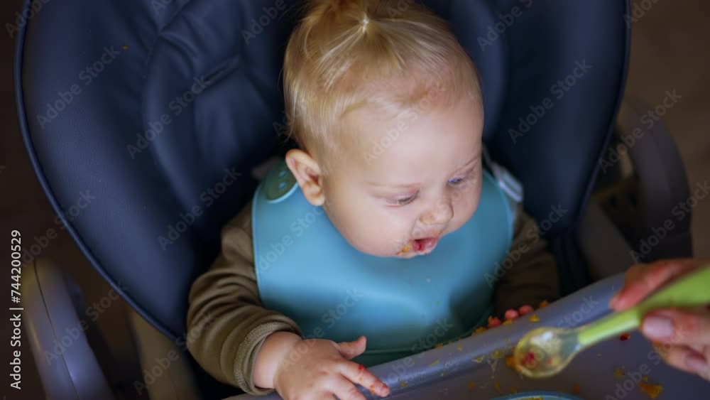 Caucasian baby boy is fed from spoon. Mother gives pureed vegetables to her son. Top view. Caucasian baby boy is fed from spoon. Mother gives pureed vegetables to her son. Top view.