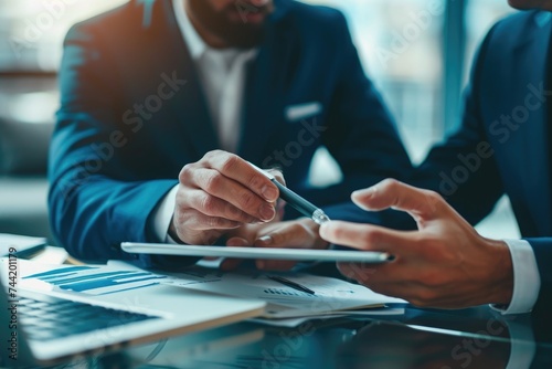 Two men are sitting at a table, actively engaged in working on a tablet device, Focused business professionals working together on a digital tablet, AI Generated
