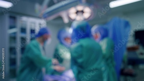 Blurred image of surgical team working in surgery room. Doctors in helmets and assisting medic perform operation on trauma. photo