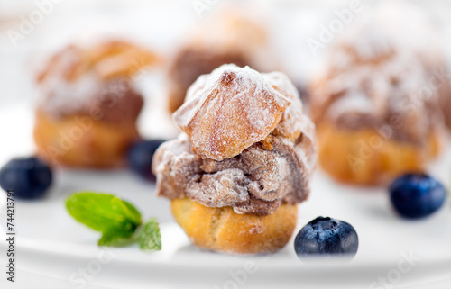 Profiterole or cream puff with filling,  powdered sugar topping with berries, on white background. Fresh homemade Cream Puffs, cake, tasty French choux puff, ecler, dessert closeup. Pastries on plate © Subbotina Anna