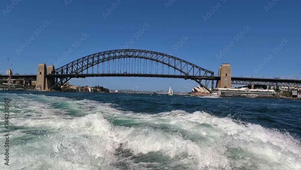 Sydney harbour bridge and opera house in distance viewed from behind boat wake