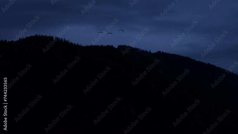 Paraglider silhouettes over Switzerland mountain at night Paraglider silhouettes over Switzerland mountain at night