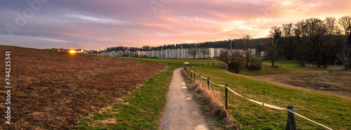 A beautiful golden hour panoramic scene in Switzerland: a walking path between fields near Katzensee lake and modern apartment buildings in Affoltern, Canton of Zurich photo