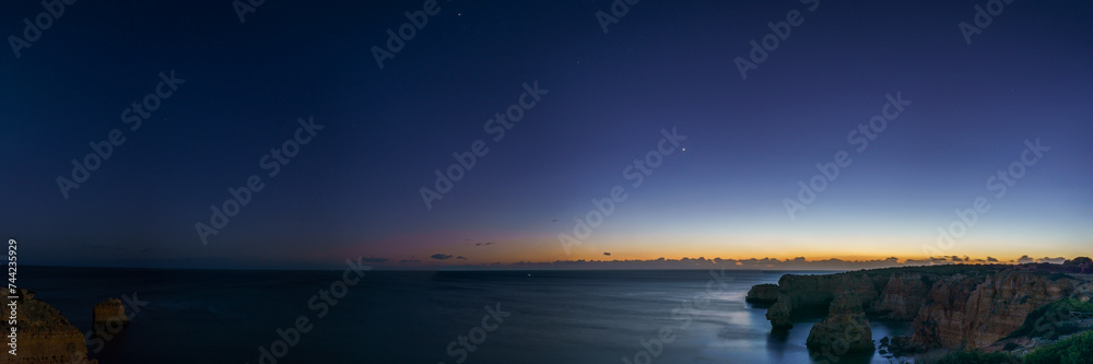 Panorama of cliffs at the coast of Atlantic Ocean during dusk with planets Venus, Saturn and Jupiter near the Cave of Benagil, Algarve, Portugal