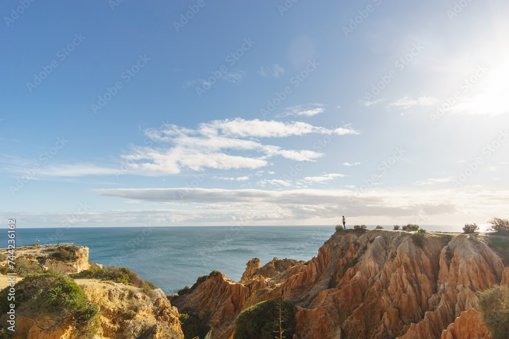 Tourist standing on golden rock cliffs at the coastline of the Atlantic Ocean with near the Cave of Benagil, Algarve, Portugal Tourist standing on golden rock cliffs at the coastline of the Atlantic Ocean with near the Cave of Benagil, Algarve, Portugal