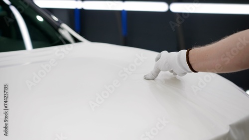 Close-up of a mechanic installing a vinyl film to protect the hood of a white car. The master sticks a white film on the car body. The master sticks a protective white film on the car door. Vehicle