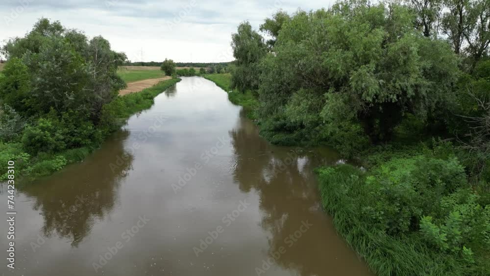 Drone flying over small lake in rural field under cloudy sky Drone flying over small lake in rural field under cloudy sky