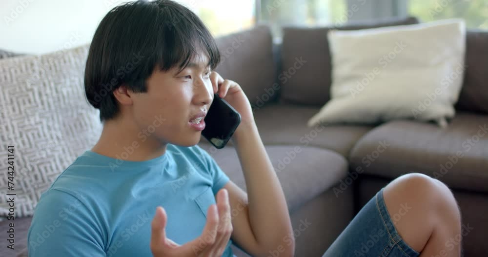 Angry teenage Asian boy talks on the phone at home Angry teenage Asian boy talks on the phone at home