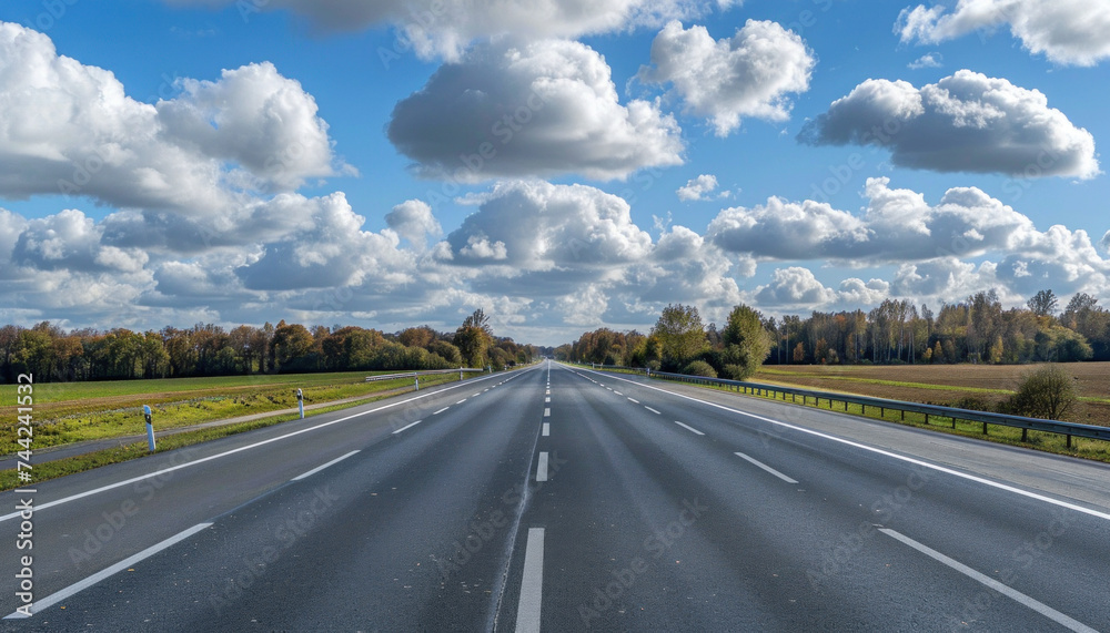 Clear asphalt road under a blue sky with fluffy clouds.