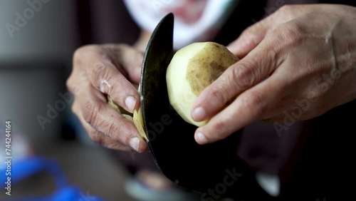 A person uses a traditional vegetable cutter to peel potatoes, prepare food for cooking, and emphasize a vegetarian diet concept. photo