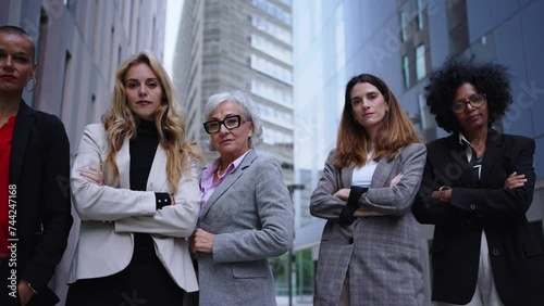 Low angle in motion female entrepreneurs in suits from empowered women business in city. Group of five serious coworkers of diverse races and ages looking confident at camera with arms crossed outdoor photo