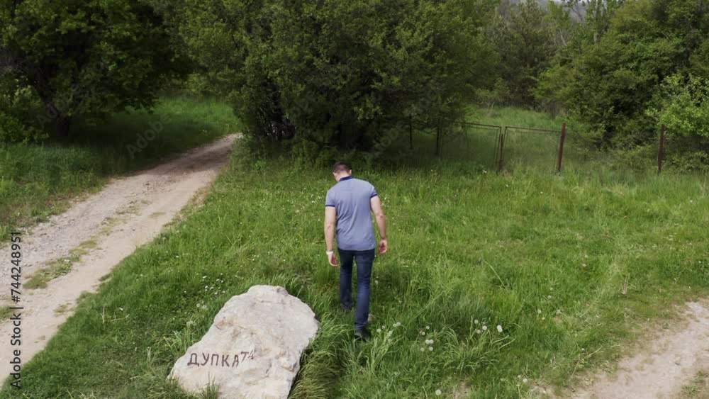 Follow through drone shot of a tourist walking in the woodlands of Tsarichina hole, passing by a rock landmark in a village in Bulgaria. Follow through drone shot of a tourist walking in the woodlands of Tsarichina hole, passing by a rock landmark in a village in Bulgaria.