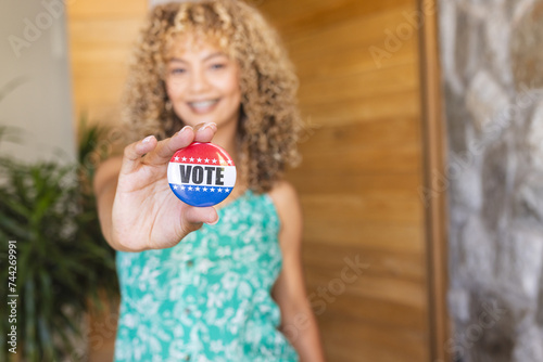 Young biracial woman holds a 'vote' badge towards the camera, with copy space