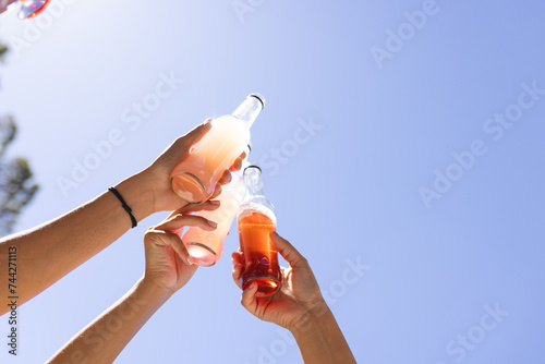 Hands clinking soda bottles against a clear blue sky photo