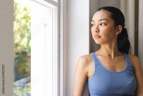 Young Caucasian woman looks thoughtfully out a window, with copy space photo