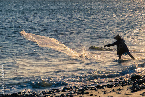 silhouette of fisherman pulling his trammel net on the beach shore, during sunset