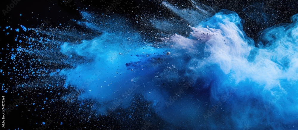 Frozen motion image of a vibrant cloud of blue and white color powder exploding on a black background, creating a mesmerizing abstract composition with glittery texture.