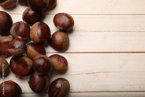 Sweet fresh edible chestnuts on light wooden table, top view. Space for text