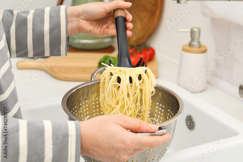 Woman with colander of cooked spaghetti and pasta server at sink, closeup photo