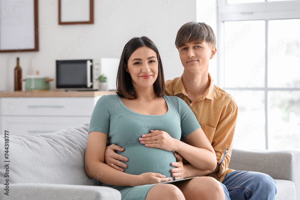 Young pregnant couple hugging on sofa at home Young pregnant couple hugging on sofa at home