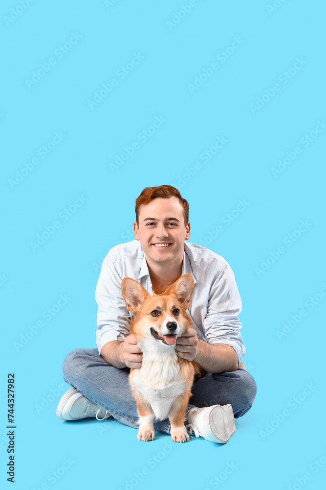 Redhead young happy man with cute Corgi dog sitting on blue background Redhead young happy man with cute Corgi dog sitting on blue background