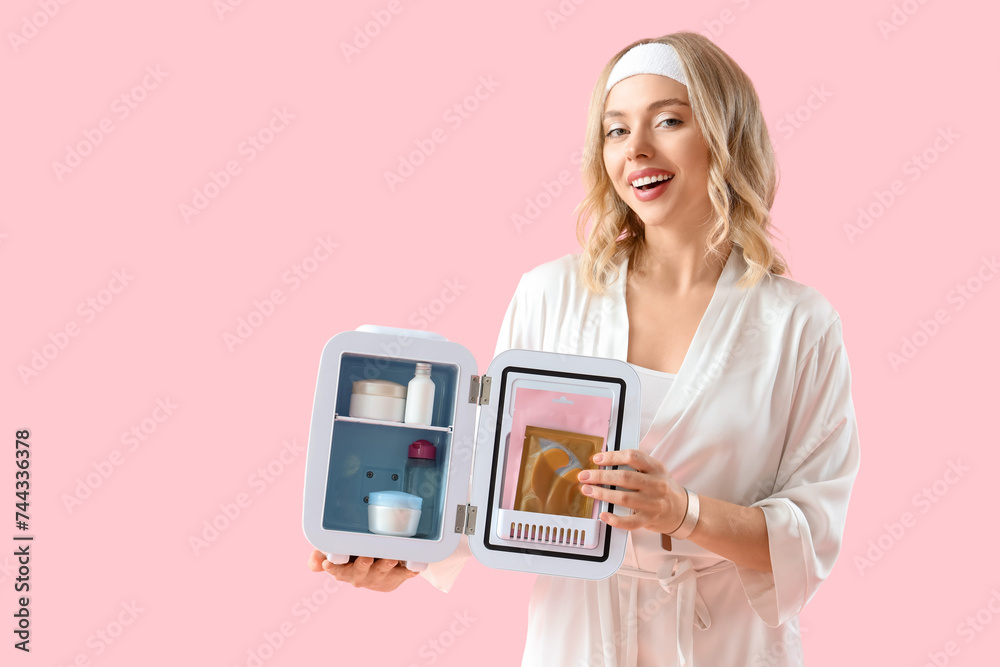 Beautiful young happy woman with small cosmetic refrigerator on pink background Beautiful young happy woman with small cosmetic refrigerator on pink background