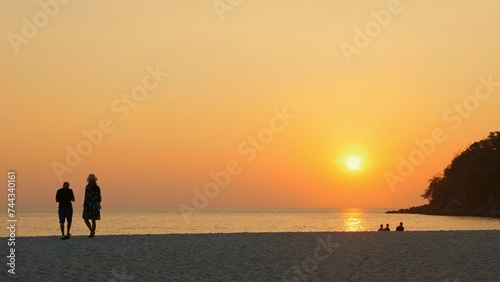 Couple enjoying peaceful walk on beach at sunset, with silhouettes against orange sky. Tranquility and connection with nature.