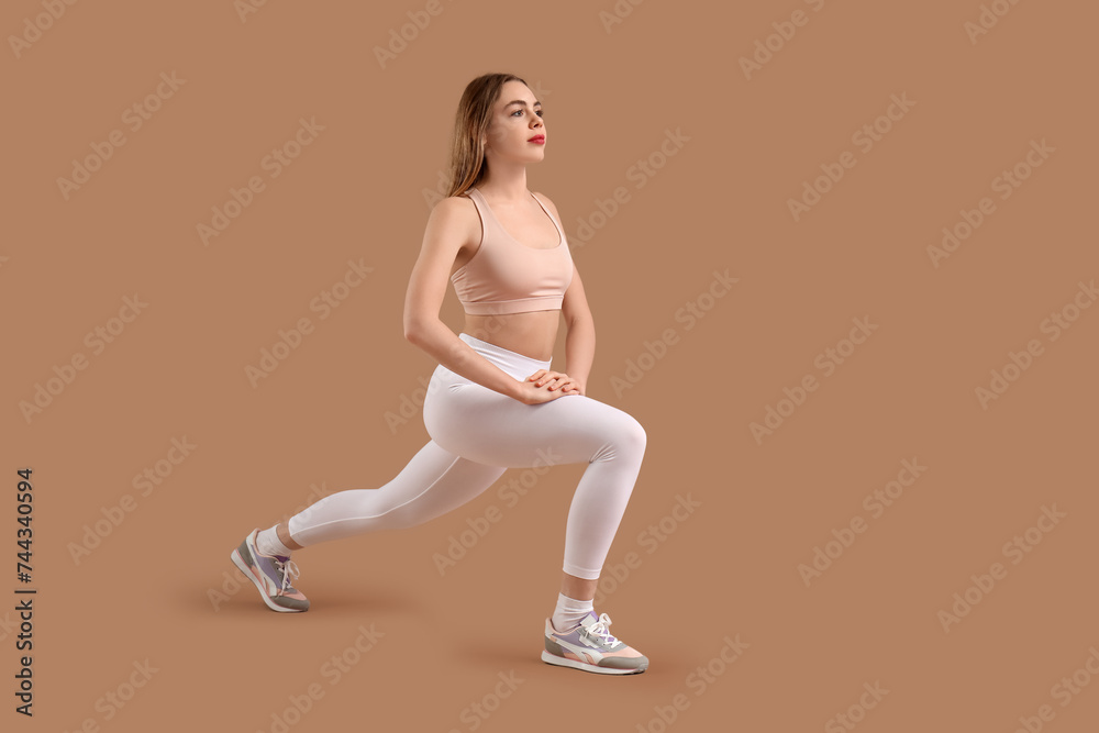 Beautiful young woman in sportswear training on brown background