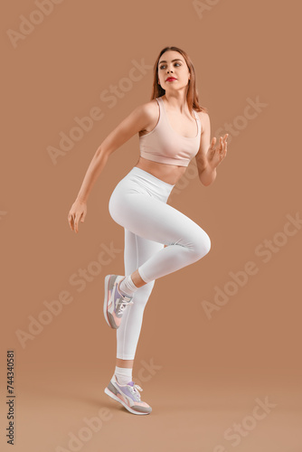 Beautiful young woman in sportswear training on brown background © Pixel-Shot