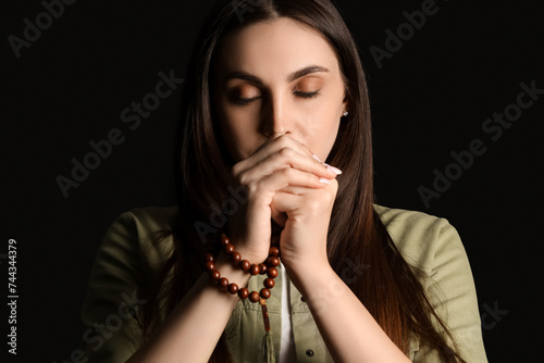 Beautiful woman praying with beads on black background  closeup