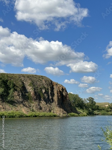 a lake with a cliff in the foreground and a blue sky with clouds in the background