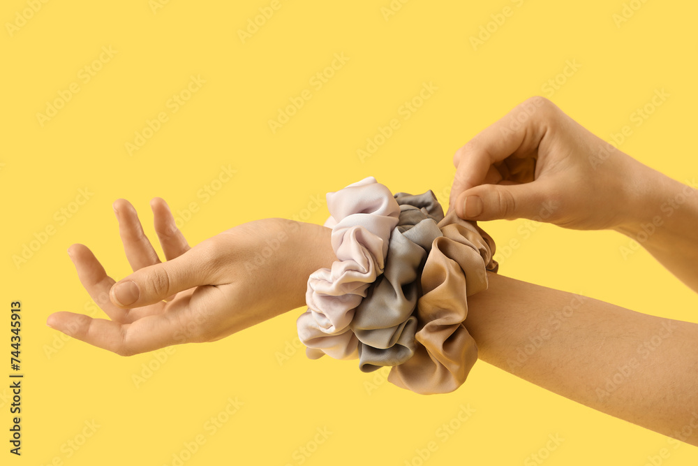 Fototapeta premium Female hands with stylish silk scrunchies on yellow background